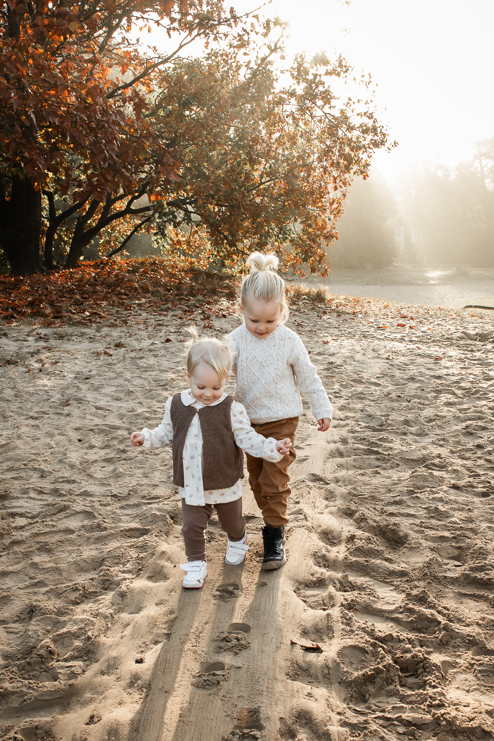 Twee peuters lopen in de ochtendzon door de duinen tijdens een gezinsshoot in de herfst